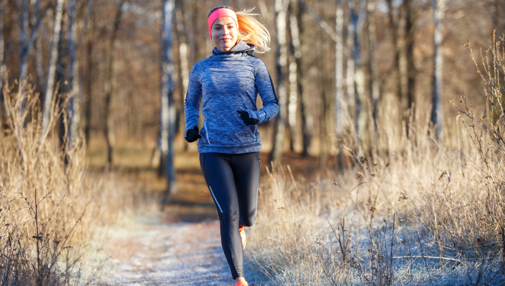 Woman running through a frosty forest trail, wearing a headband and winter athletic wear during a morning workout.